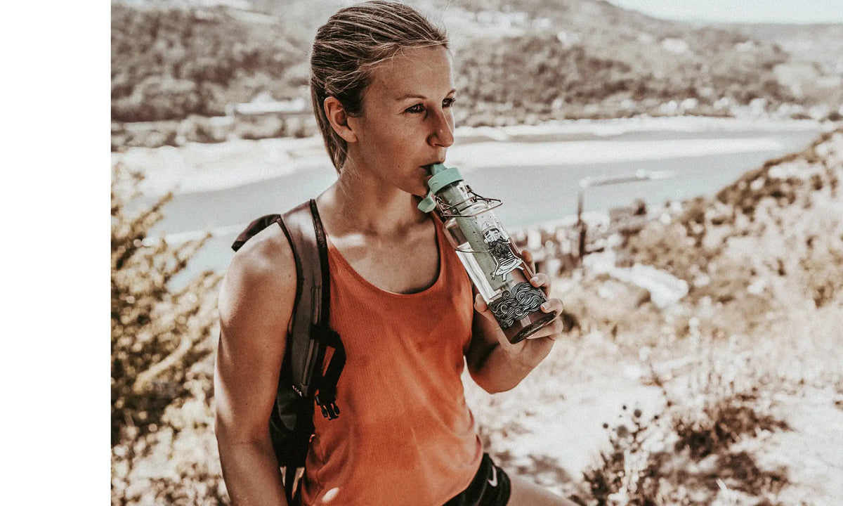Frau beim Wandern mit Glastrinkflasche und integriertem Wasserfilter trinkt