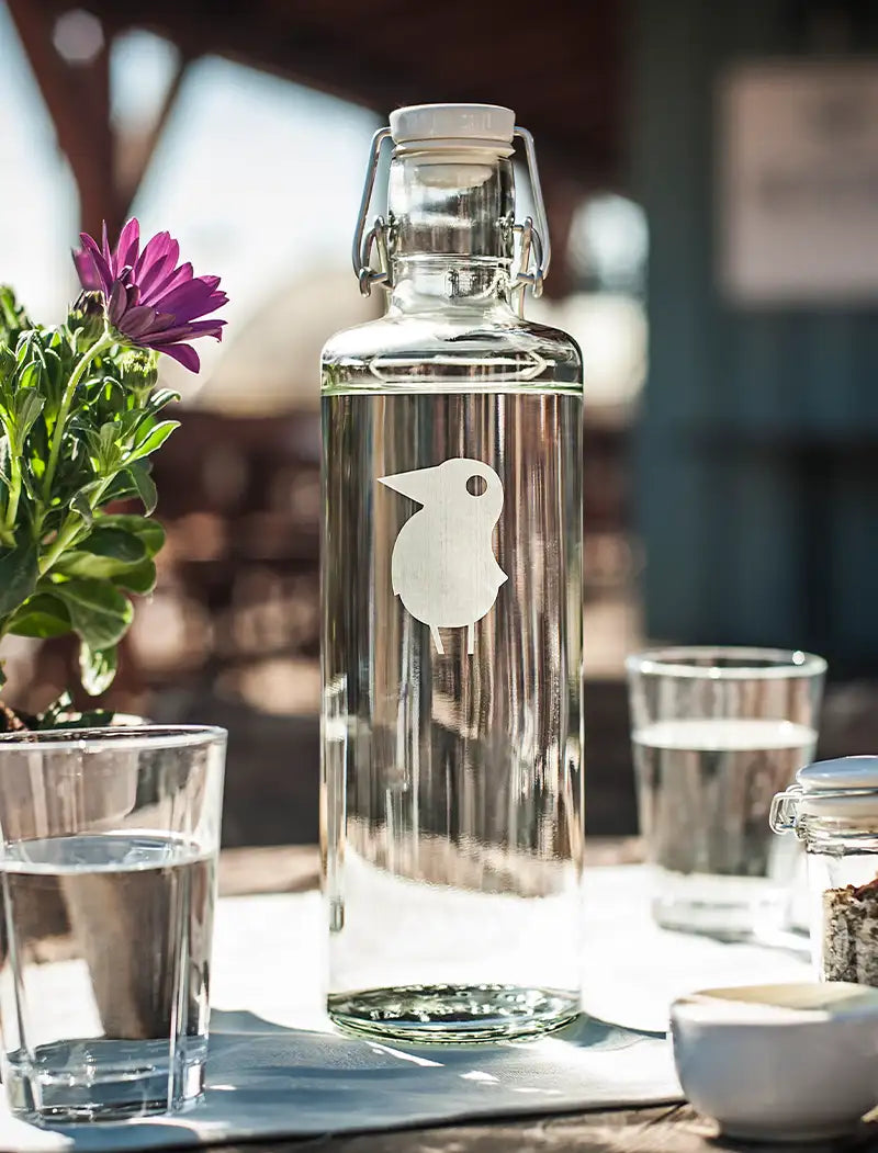 Trinkflasche aus glas mit Gravur Logo steht auf gedecktem Tisch